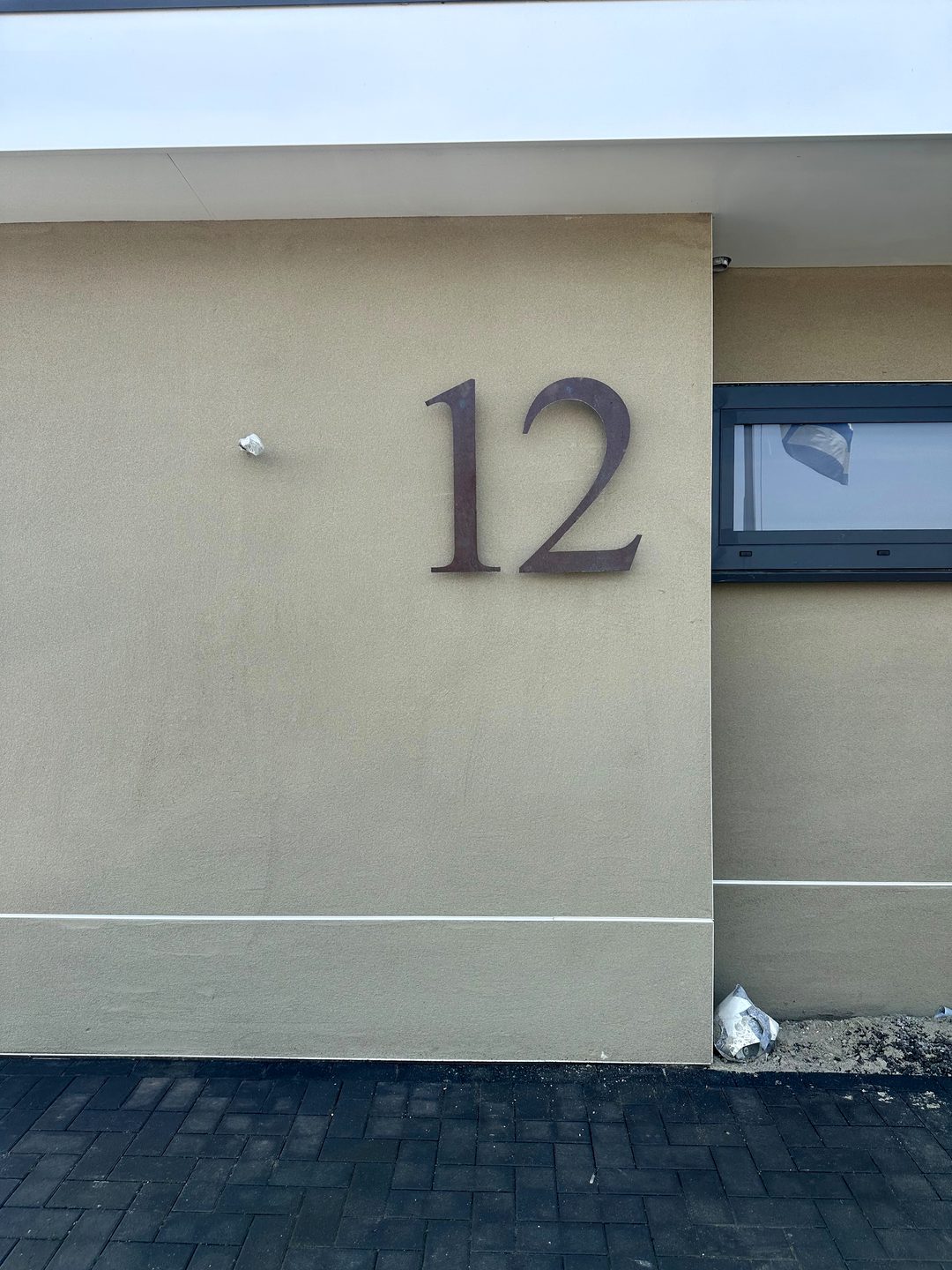 Dezelfde voorgevel van de bungalow na het stucwerk, met huisnummer en strakke plintlijn