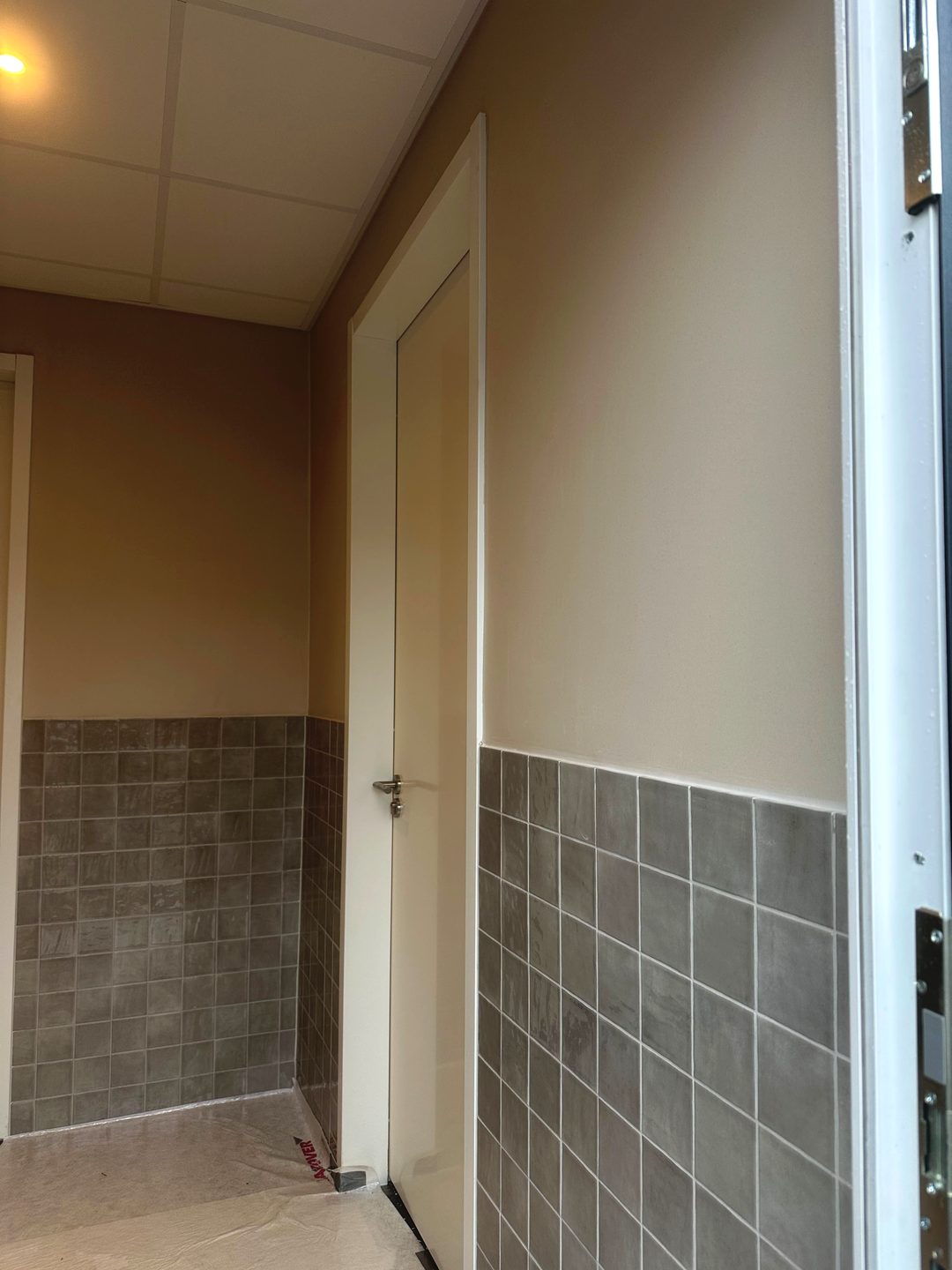 Afgewerkte wanden in een ruimte met halfhoog tegelwerk en deur