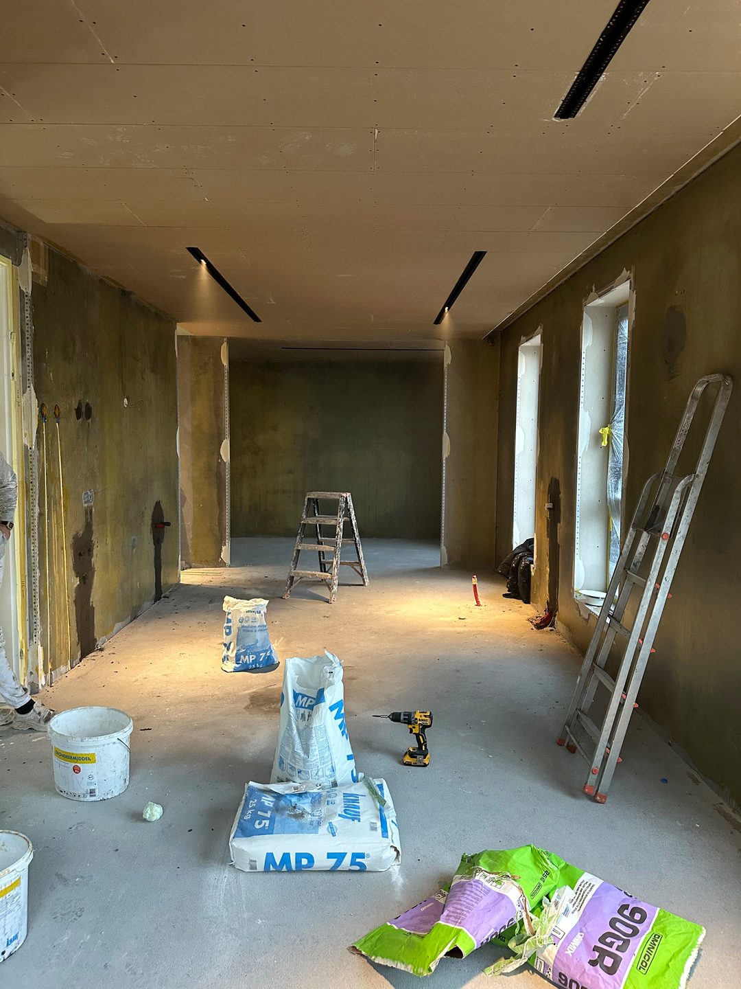 Grote ruimte vóór het stucwerk, met zakken stucmortel en ladders